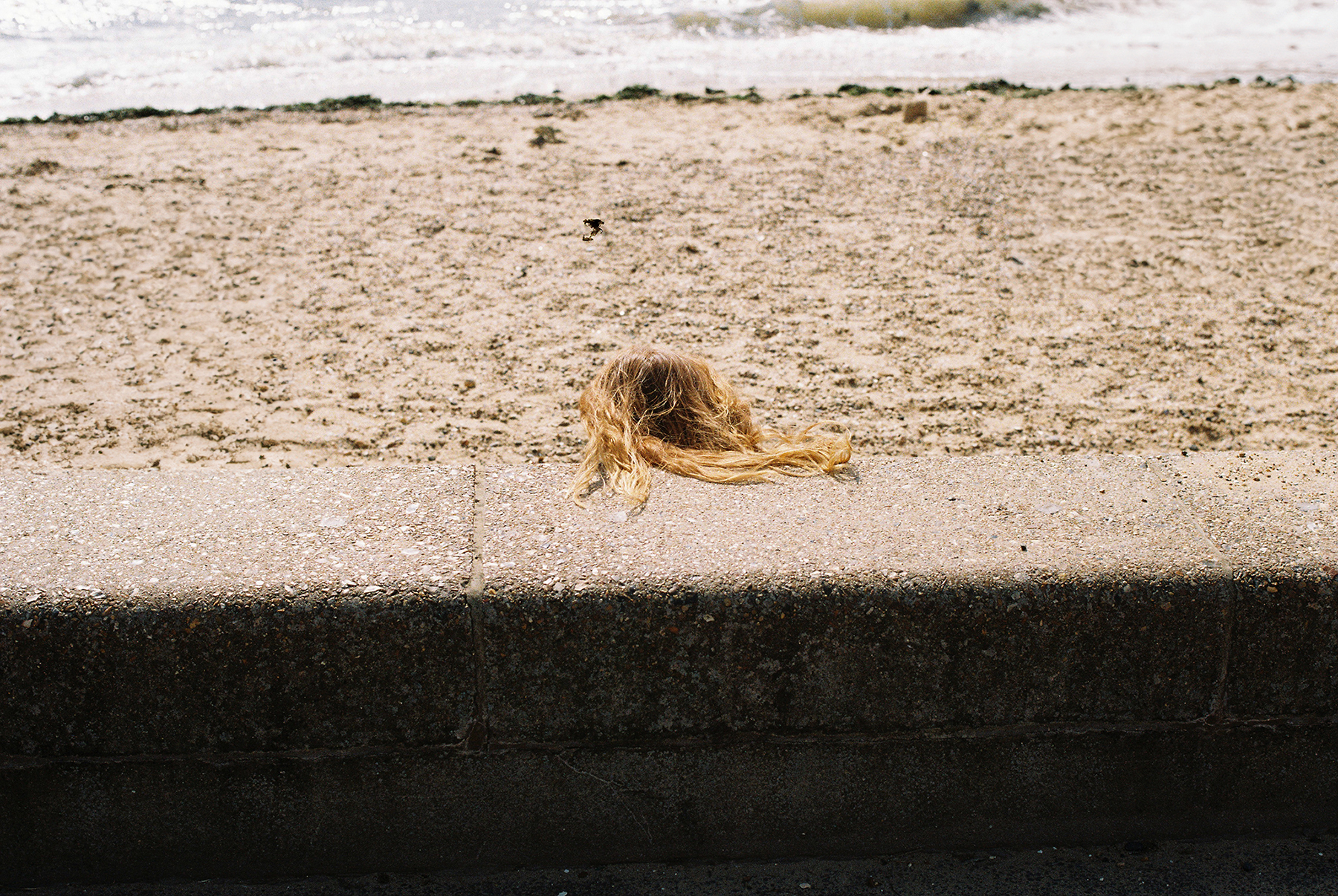 A woman with only her long hair visible resting on a sea wall on the beach.
